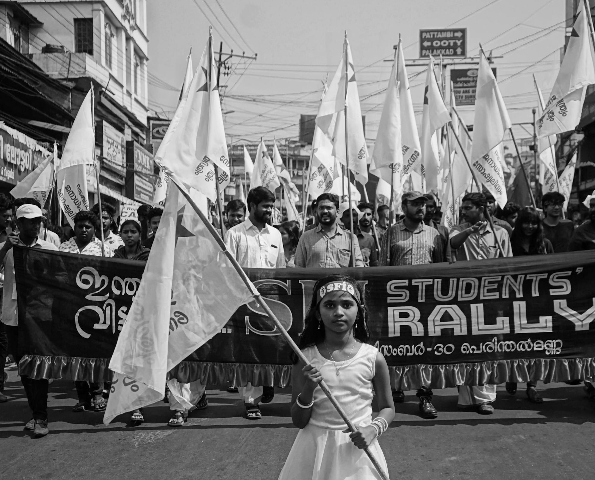 grayscale photography of girl holding banner while walking on street near crowd of people